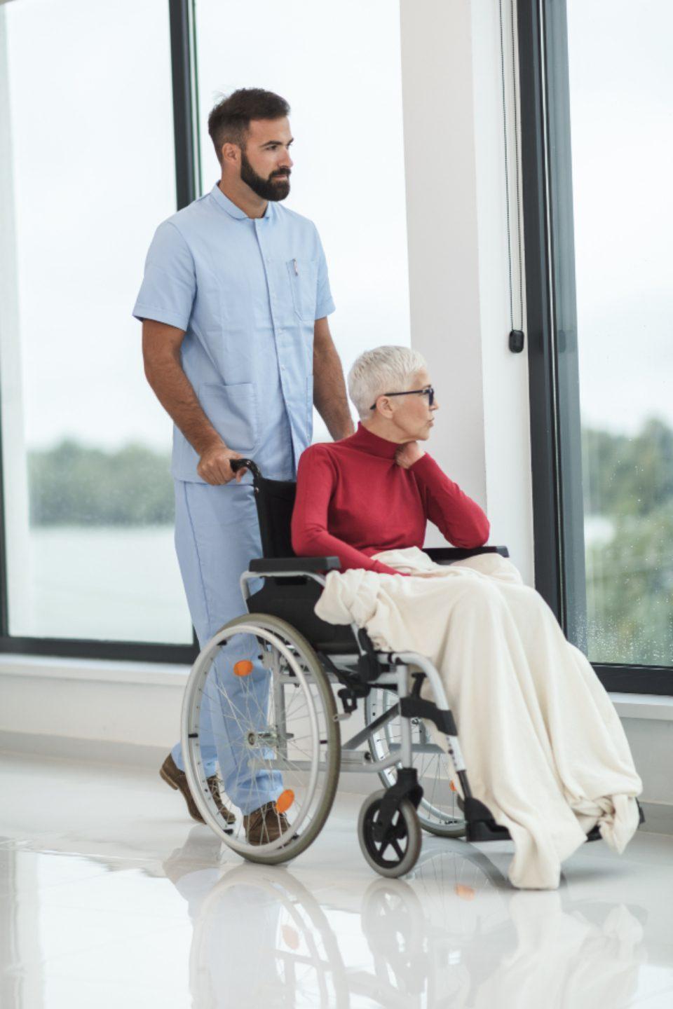 A support worker accompanying a woman using a wheelchair along a bright hospital corridor